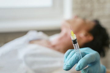 A syringe in the hands of a cosmetologist in focus. patient lying on a background blurred.