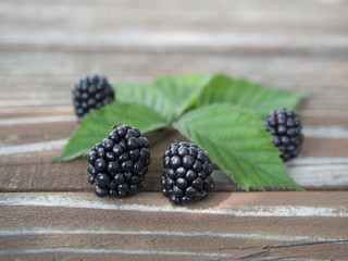 A few blackberries surrounded by green leaves lying on the wooden table.