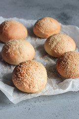 Fresh homemade burger buns with sesame seeds on grey concrete background. Concept of burger and homemade food. Dinner bread rolls or mini challah.