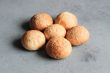 Fresh homemade burger buns with sesame seeds on grey concrete background. Concept of burger and homemade food. Dinner bread rolls or mini challah.