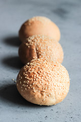 Fresh homemade burger buns with sesame seeds on grey concrete background. Concept of burger and homemade food. Dinner bread rolls or mini challah.