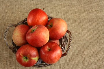 Czerwone jabłka w koszyku na tkaninie z juty © Monika