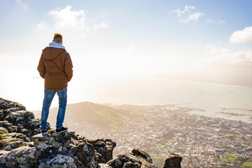 Young man is sitting on rock at Table Mountain and looking at Cape Town, South Africa