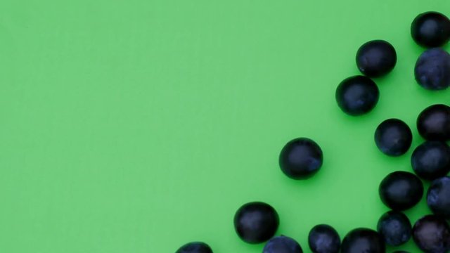 Runde frische reife Pflaumen rollen in das Standbild. Sie bedecken einen gr&uuml;nen Hintergrund, der f&uuml;r chroma keying geeignet ist. Aufnahme in Echtzeit von oben.