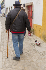 walk of a man in a hat with a small dog on the street of the old town of Obidos