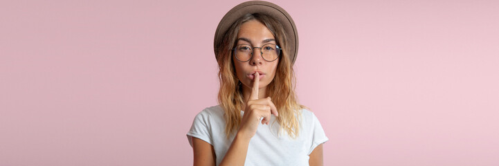 young woman shows Finger to Mouth isolated over pink background