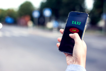 Male hand with smartphone on blurred road background. Taxi service application on screen.
