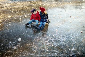 Two happy sisters playing with ice blocks by frozen river during an ice break. Children having fun in winter.