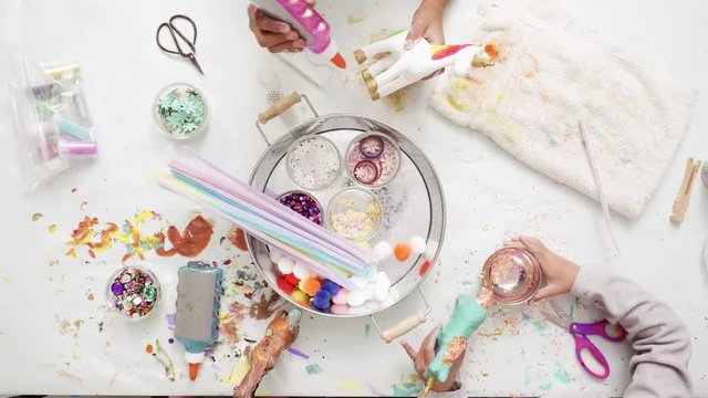Step by step. Little girls decorating paper mache unicorn with glitter and paper flowers