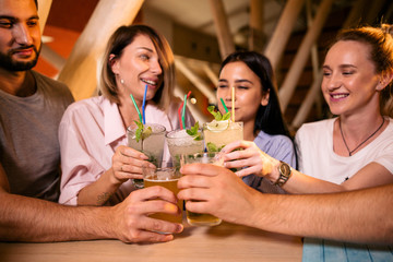 Five cheerful friends sit at the table drinking alcohol
