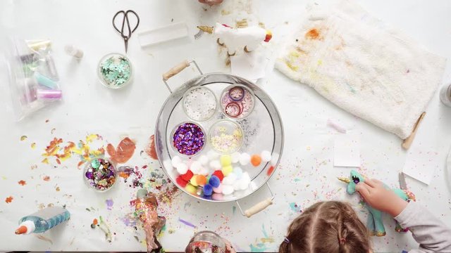 Step by step. Little girls decorating paper mache unicorn with glitter and paper flowers