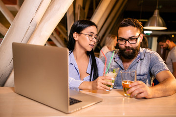 Couple drinking drinks watching a sports match on the laptop at the table in the tavern