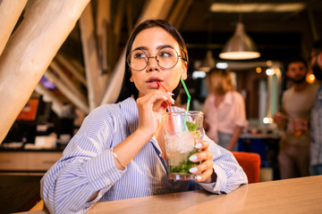 Young beautiful girl standing at the bar drinking a cocktail