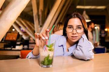 Young beautiful girl with glasses at the bar with a glass of cocktail