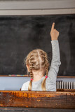Concept of public primary school education with young girl raising her hand in the classroom