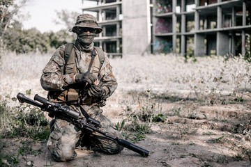 Military soldier in camouflage sitting on the ground with a rifle in his hands