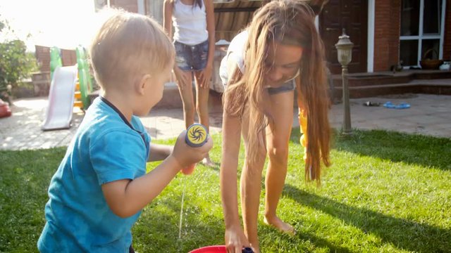 4k footage of happy laughing toddler boy shooting with water in two elder sister from toy gun