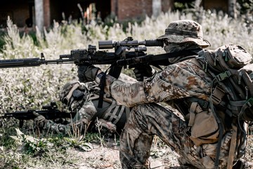 Snipers in camouflage disguise in the grass taking a fighting position for shooting