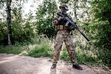 Soldier in camouflage uniform with a rifle head of the forest area