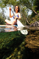 Over and Under picture of a woman paddle boarding in a river during a vibrant sunny summer day. Taken near Tofino and Ucluelet, Vancouver Island, BC, Canada.