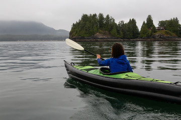 Girl kayaking in the ocean during a cloudy and gloomy sunrise. Taken in Tofino, Vancouver Island, BC, Canada.