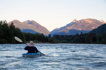 Kayaking in a river surrounded by Canadian Mountains during a vibrant summer sunset. Taken in Squamish, British Columbia, Canada.