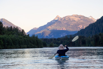 Fototapeta na wymiar Kayaking in a river surrounded by Canadian Mountains during a vibrant summer sunset. Taken in Squamish, British Columbia, Canada.