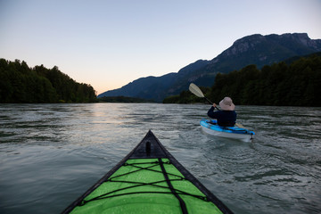 Fototapeta premium Kayaking in a river surrounded by Canadian Mountains during a vibrant summer sunset. Taken in Squamish, British Columbia, Canada.