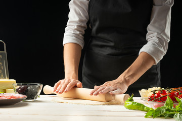 Raw pizza ingredients on a wooden table, the chef prepares pizza on a dark background