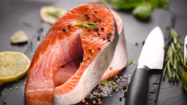 Salmon. Raw trout fish steak with herbs and lemon rotated on slate. Cooking, seafood. Healthy eating concept. Rotation. Slow motion 4K UHD video 3840x2160