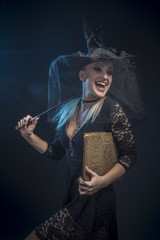 Young witch with a wand and a spellbook casting a spell in her ritual, halloween concept