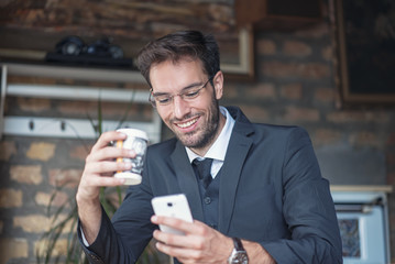 Happy young businessman chatting on his cell phone, having a to go coffee in an outdoor cafe