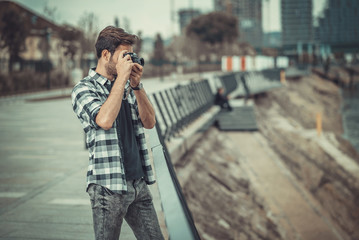 Young attractive man, a photographer, taking photographs in an urban area with an analog SLR camera