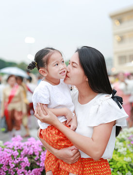 Portrait of happiness mother carrying little kid girl in arms at traditional thai festival outdoor.