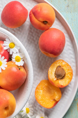 Delicious ripe apricots in a bowl on the wooden table. Close-up with apricots and daisy flowers