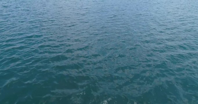 Aerial top to bottom very low over blue water flying forward.  Camera tilts to straight down causing a vertigo effect as the drone flys forward.