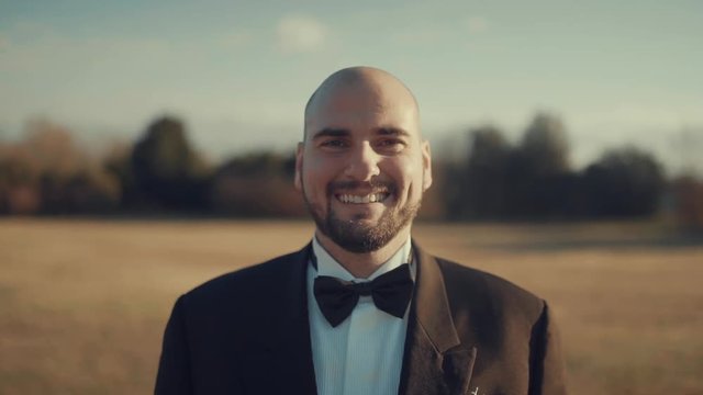 Portrait of Elegant Man smiling at camera dressed with a classy smoking and papillon, slow motion of a smile at sunset