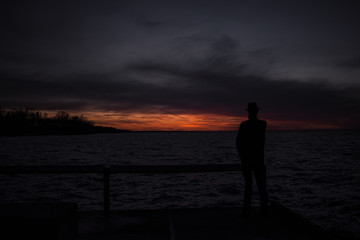 Fototapeta premium Mysterious silhouette man on the peer at sunset