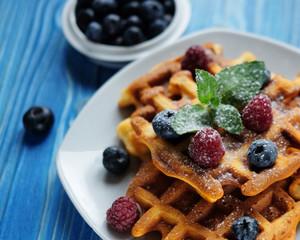 Traditional belgian waffles with fresh berrys and sugar powder on white plate, blue wooden background. Flat lay, top view, copy space.