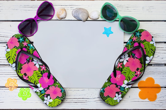 Beach flat lay with brightly patterned flip flops and sun glasses and sea shells on a white painted wooden background - room for copy