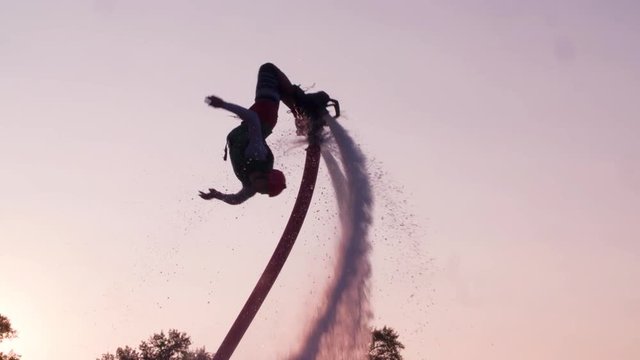 Flyboarder doing flip tricks slow motion flying Flyboarding medium shot video on sunset backlight