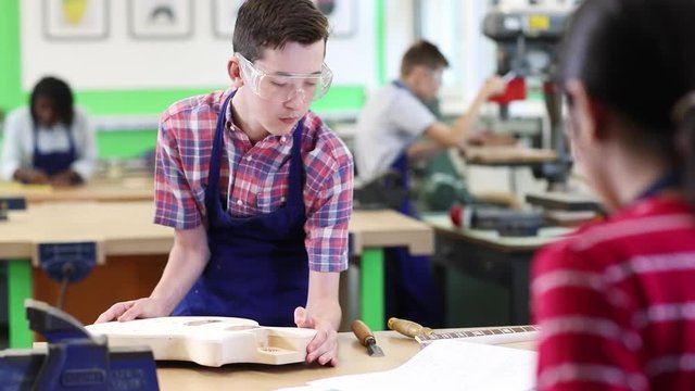 Male High School Student Building Guitar In Woodwork Lesson