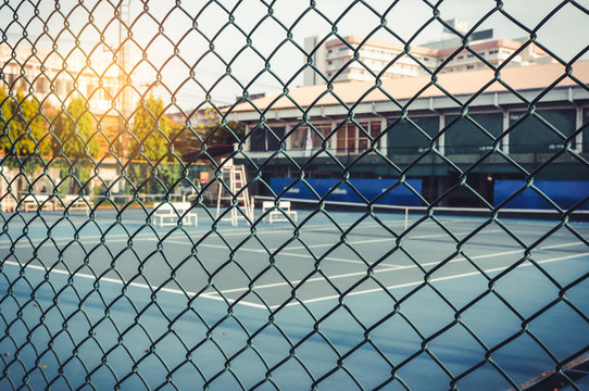 Metal mesh wire fence with tennis court in blurry for background.