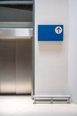 Blue signage on white wall background in front of elevator
