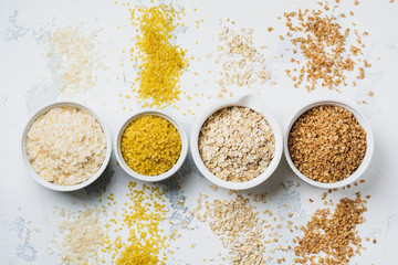 Variety of cereal flakes rice, millet, buckwheat, oatmeal. Superfood in white ceramic bowls on light wooden background. Top view.