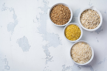 Variety of cereal flakes rice, millet, buckwheat, oatmeal. Superfood in white ceramic bowls on light wooden background. Top view.