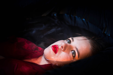 Close up portrait of a beautiful young woman blue eyes red lips floating in black water