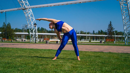 Naklejka premium Girl on street workout makes slopes to sides. She is standing barefoot on lawn. Yoga outdoors. Healthy lifestyle.