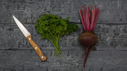 Fototapeta na wymiar Fresh red beetroot and a bunch of parsley and knife on a table. The view from the top. Flat lay.