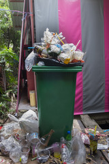 Green garbage can and pile of garbage in market.